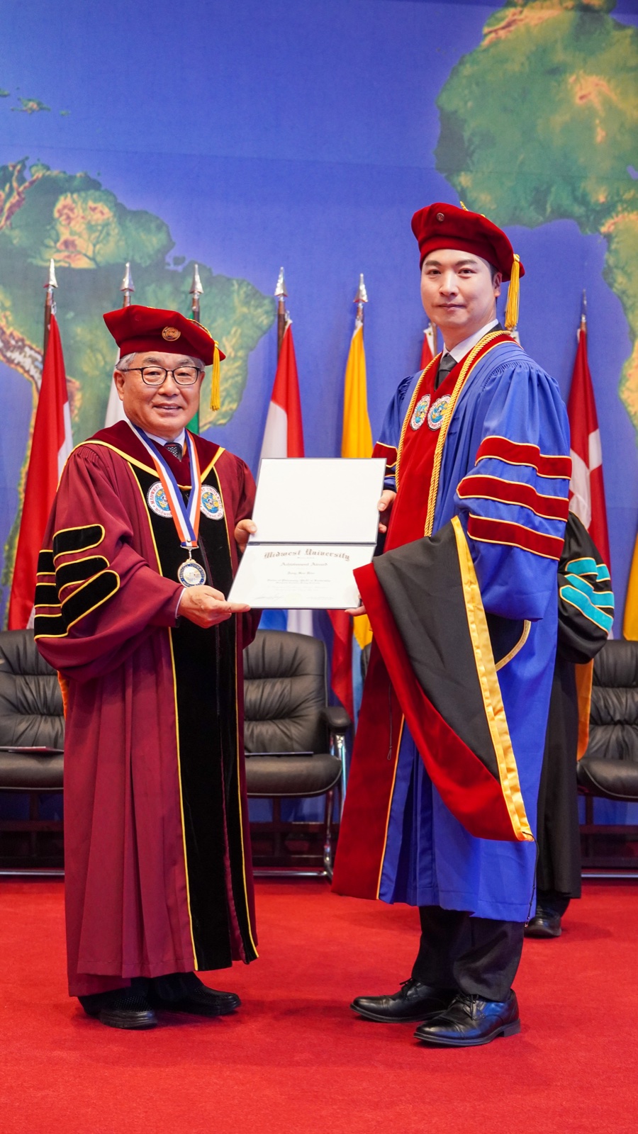 Jungsoo Kim receiving the Achievement Award certificate on stage from a university official during the commencement ceremony