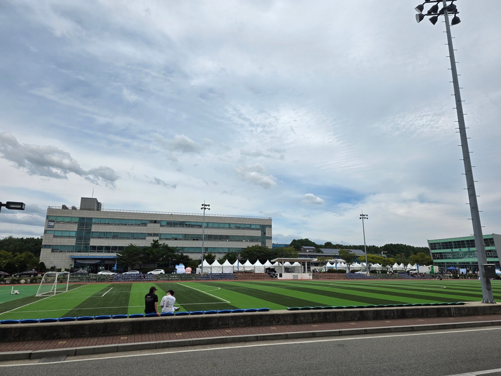 The GTEC athletic field on the day of the Siheung Career Fair, with white marquees lining its far side in front of the main buildings