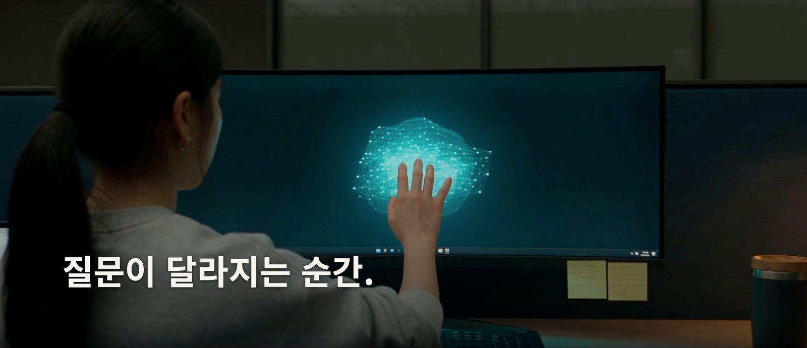 A still from the promotional video: a student reaching toward a glowing sphere of light inside her monitor, with the caption 'The moment the question changes'