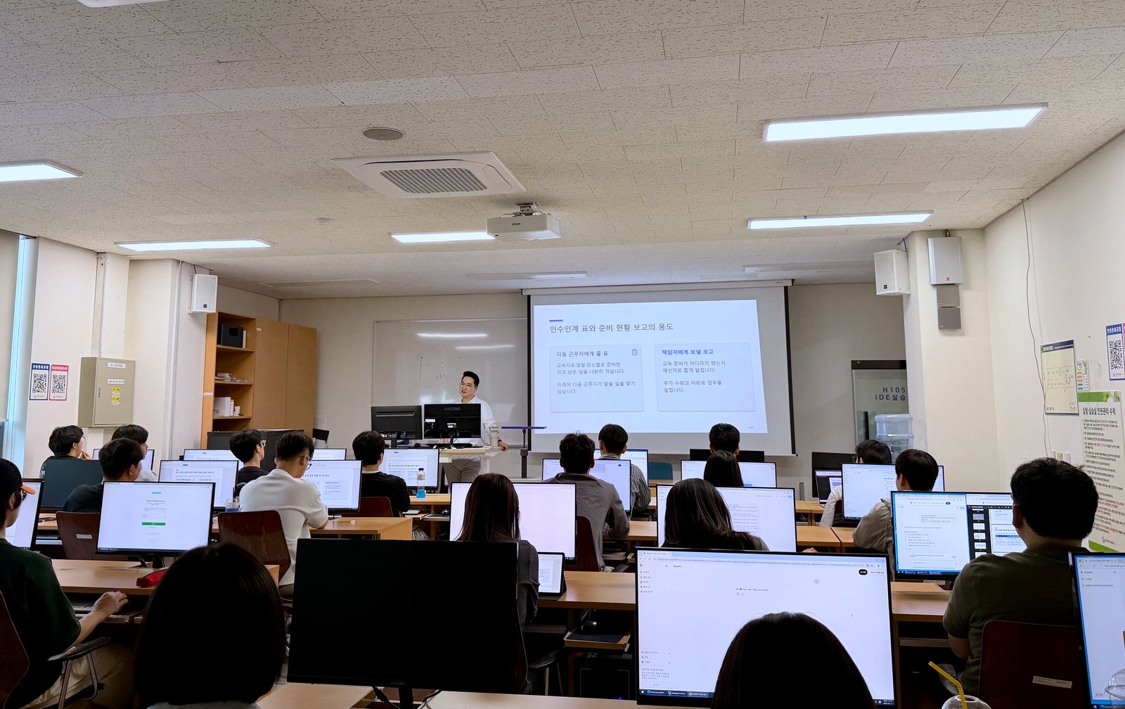 Bootcamp participants in GTEC’s H105 IDE lab, each with ChatGPT open, as the slide sets the exercise: handover tables and readiness reports