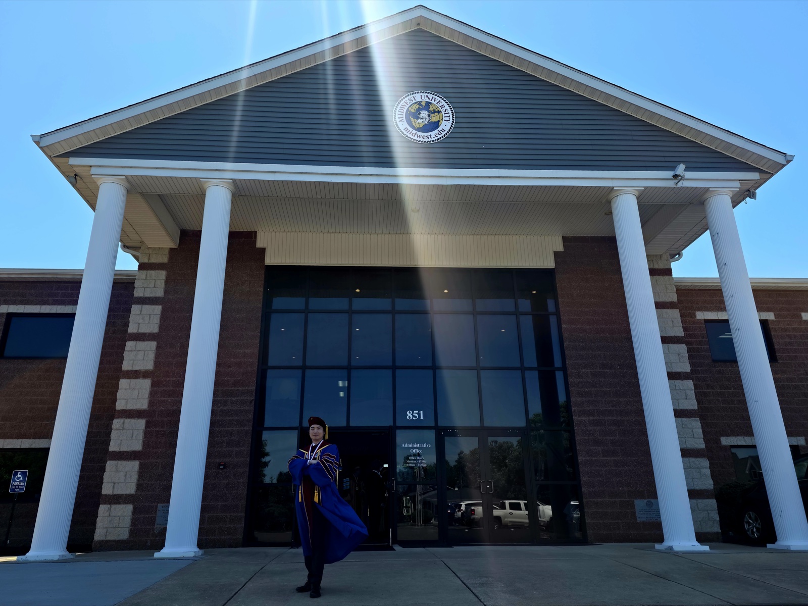 Jungsoo Kim in doctoral regalia in front of the Midwest University administrative building, 14 May 2026