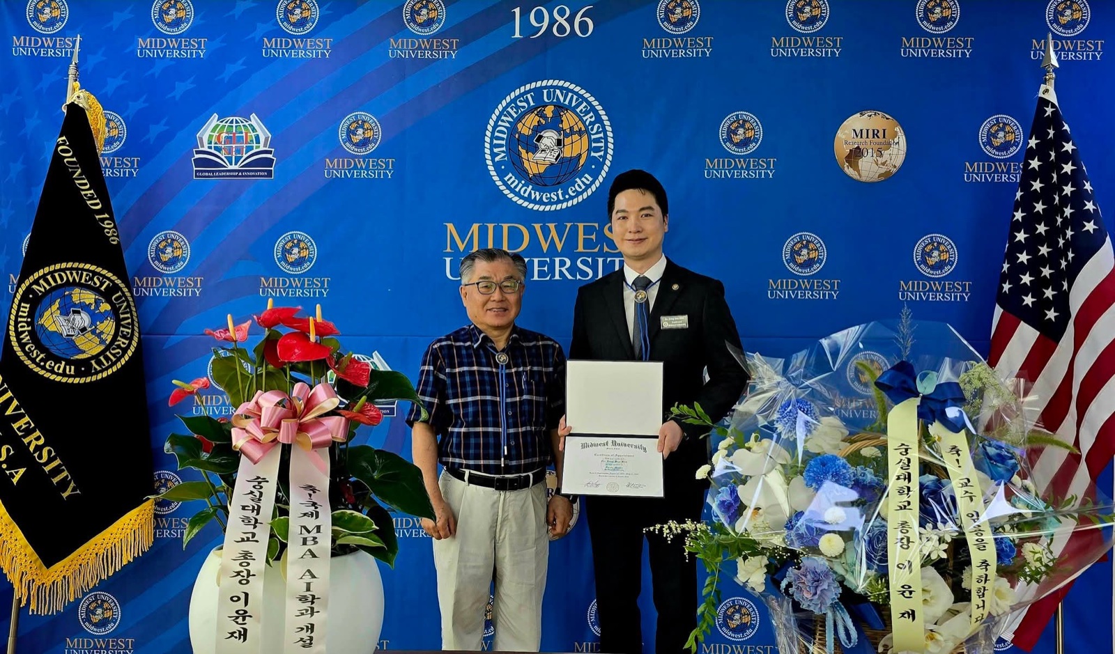 Jungsoo Kim holding a certificate from Midwest University beside a university official, in front of the Midwest University backdrop